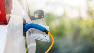 Nahaufnahme des Elektroauto-Einlasses mit angeschlossenem Ladekabel auf grünem Hintergrund