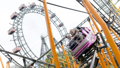 Personen in einer Achterbahn im Wiener Prater, im Hintergrund das Riesenrad