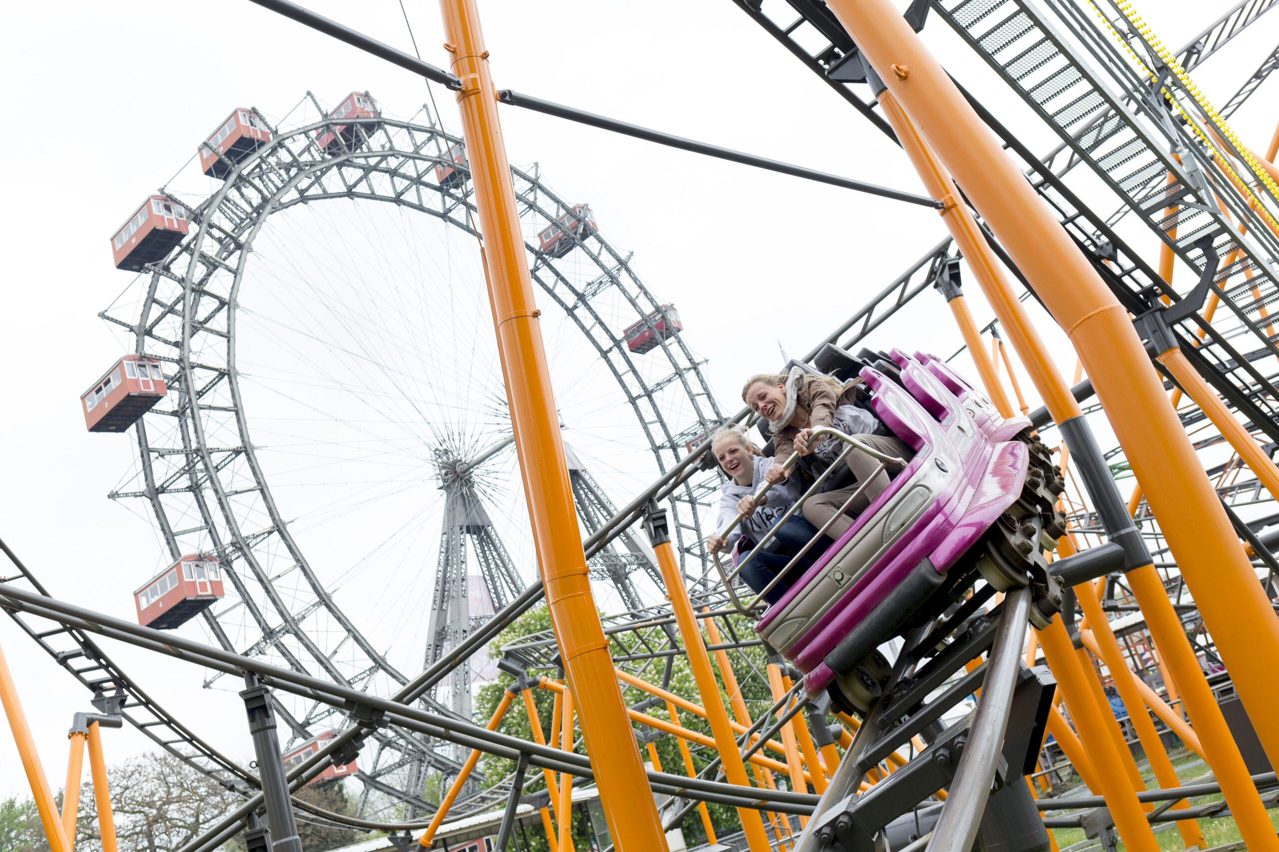 Personen in einer Achterbahn im Wiener Prater, im Hintergrund das Riesenrad