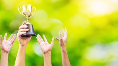 Viele Hände hoben sich. Der Sieger hält den Pokalpokal in der Hand. auf verschwommenem grünem Hintergrund"