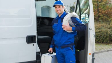 Ein Mann im Blaumann steht mit Werkzeugkoffer und Kabel vor seinem Auto.