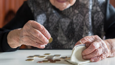 Ältere 95-jährige Frau, die elend zu Hause am Tisch sitzt und nach dem Bezahlen der Rechnungen die restlichen Münzen aus der Rente in ihrer Brieftasche zählt.