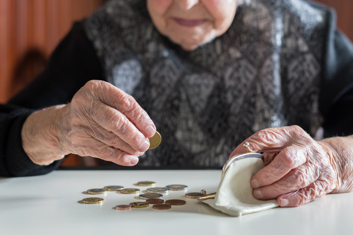 Ältere 95-jährige Frau, die elend zu Hause am Tisch sitzt und nach dem Bezahlen der Rechnungen die restlichen Münzen aus der Rente in ihrer Brieftasche zählt.