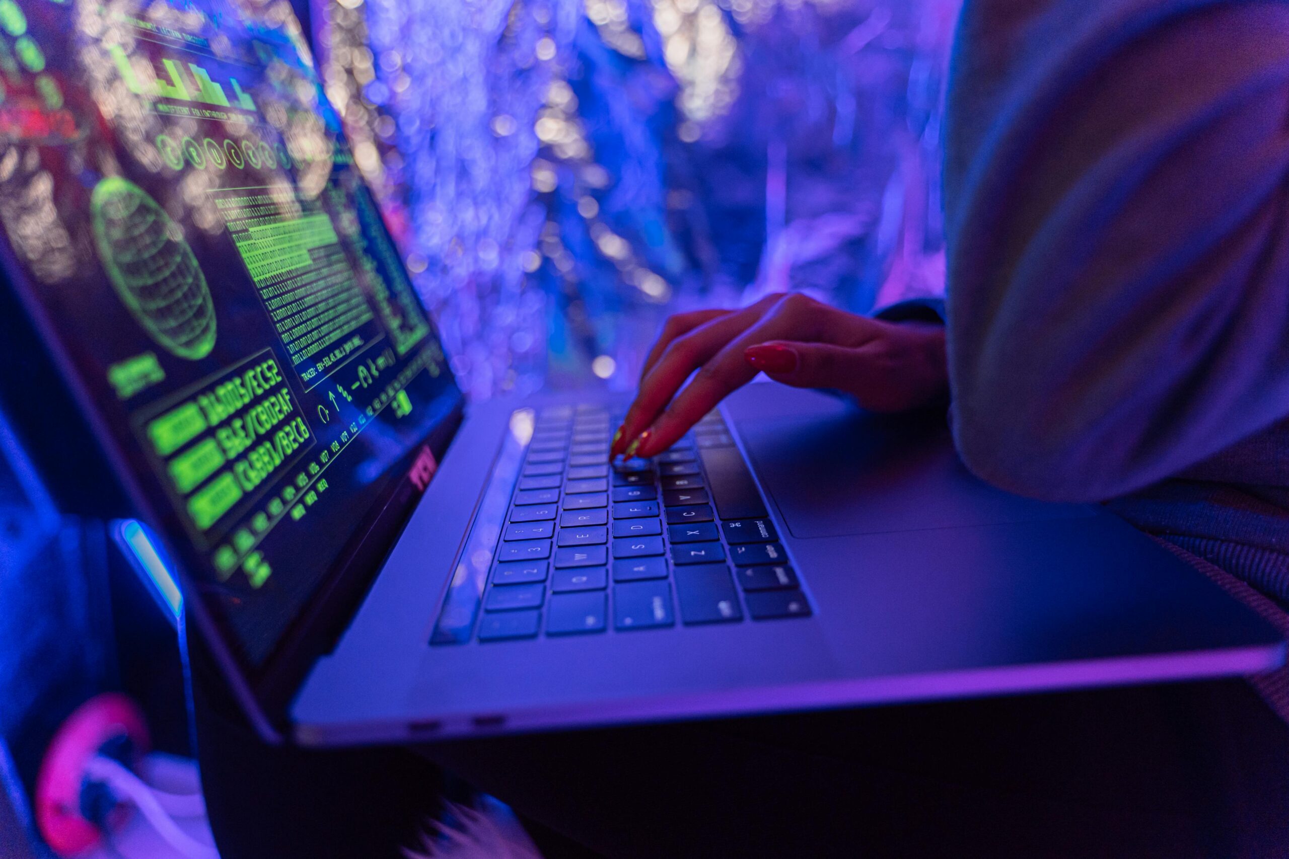 Cyberangriff dargestellt durch Hand auf Tastatur eines Laptops und grünem Code auf dem Bildschirm in einem blau-violett erleuchteten Zimmer