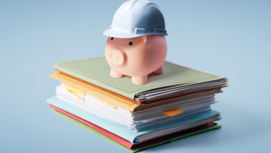 Sparschwein auf Papierstapel mit Schutzhelm