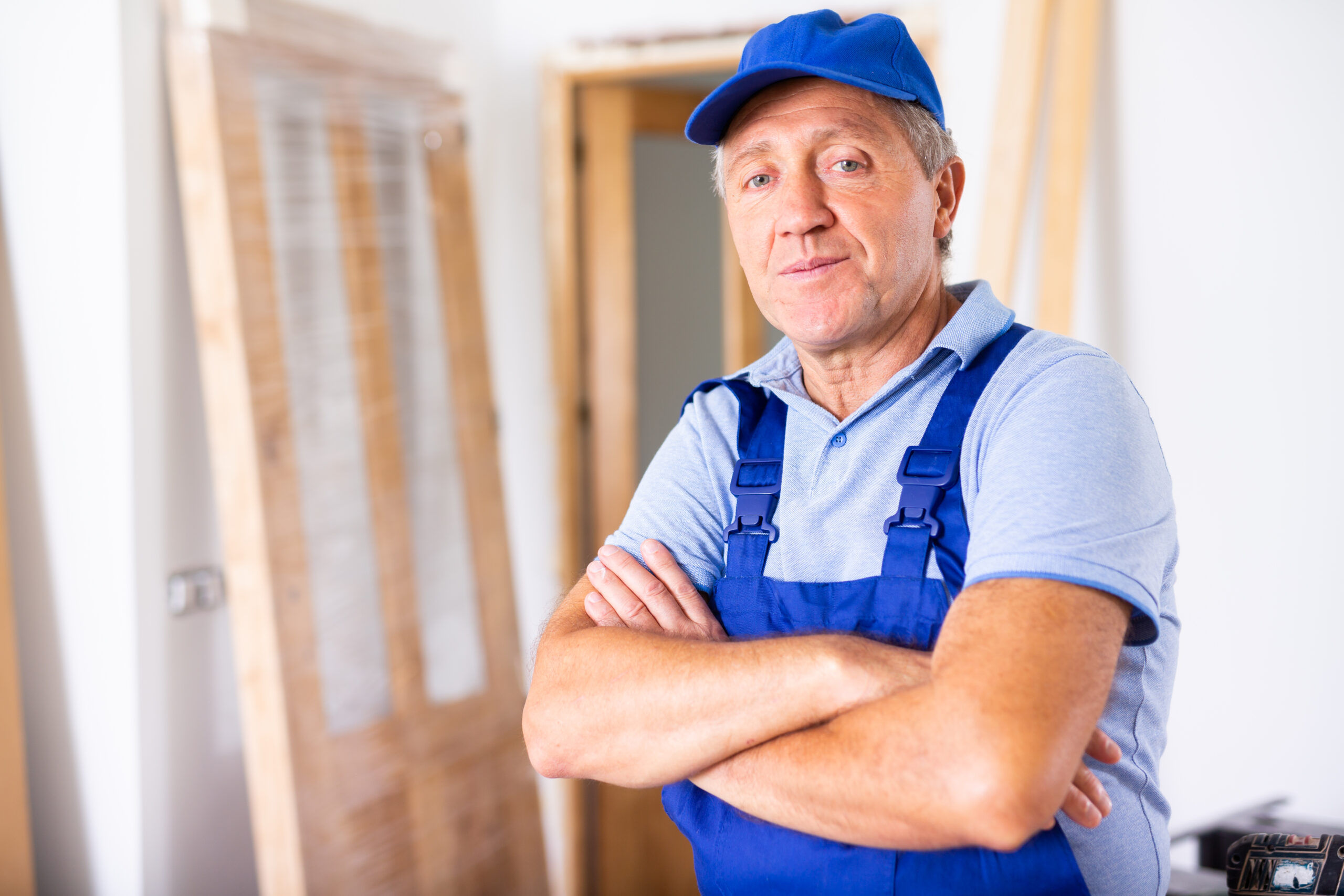 Portrait of a confident male builder in uniform looking at camera with crossed hands on chest during renovation at home