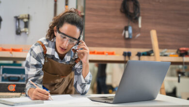 Tischlerin vor PC und am Handy telefonierend in der Werkstatt
