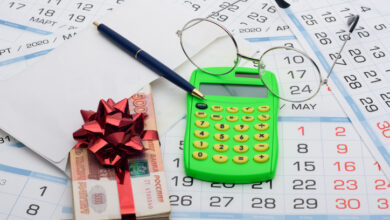 Geldstapel mit Geschenksschleife auf Tisch mit Dokumenten und Taschenrechner