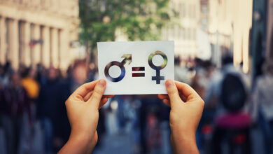 Gender equality concept as woman hands holding a white paper sheet with male and female symbol over a crowded city street background. Sex sign as a metaphor of social issue.