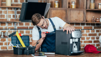 professional young worker in eyeglasses and protective workwear fixing coffee machine