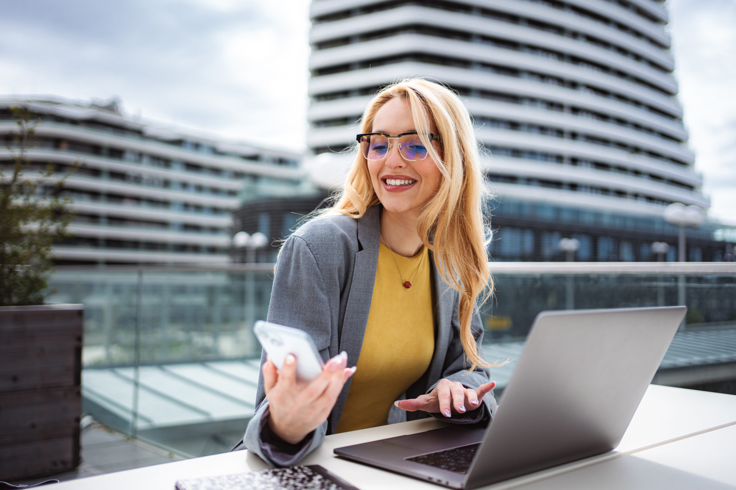 Young businesswoman remote working outdoors with laptop and phone